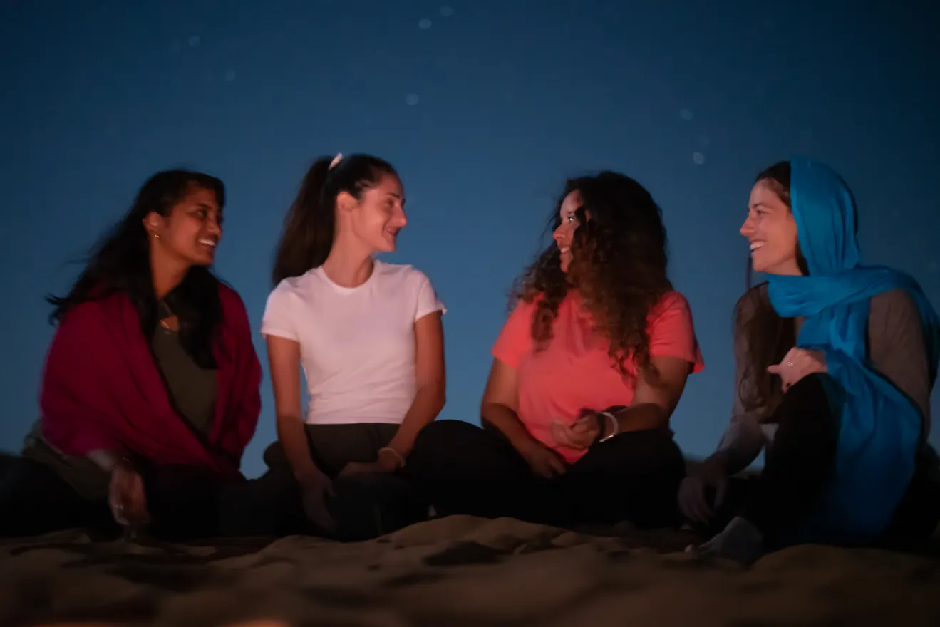 ארבע מטיילות יושבות על חול המדבר תחת שמי הלילה